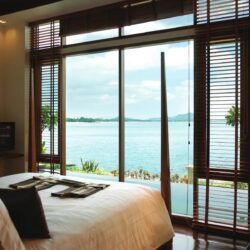 Sea Front Pool Villa Seaview - The Sarann Koh Samui, Thailand The Sarann Koh Samui's Sea Front Pool Villa Seaview features a white-lined bed, floor-to-ceiling windows with wooden blinds, and a view of a private pool and the turquoise sea horizon.